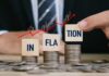 Blocks spelling 'INFLATION' placed on stacks of coins with a rising graph in the background
