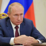 Vladimir Putin in a suit sits at a table.