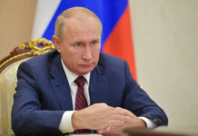 Vladimir Putin in a suit sits at a table.