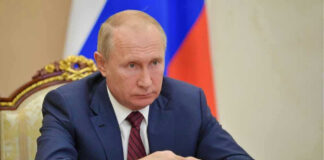 Vladimir Putin in a suit sits at a table.