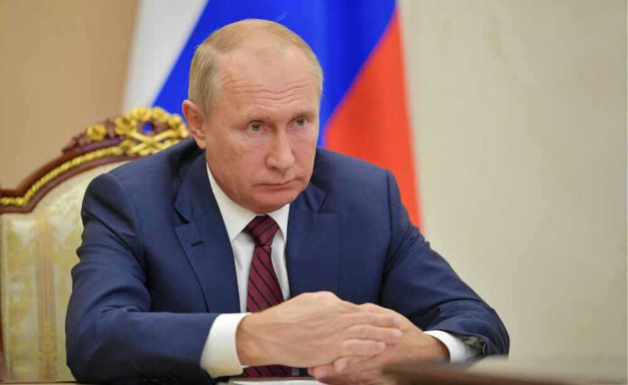 shutterstock_2329478503 Vladimir Putin in a suit sits at a table.