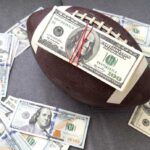 Football with a stack of U.S. hundred-dollar bills secured by rubber bands