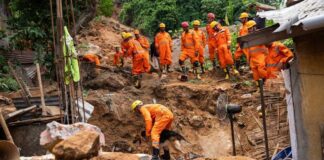 Rescue workers in orange uniforms search a landslide site with a dog