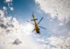 A yellow helicopter flying against a backdrop of clouds and sunlight