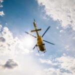 A yellow helicopter flying against a backdrop of clouds and sunlight