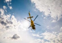 A yellow helicopter flying against a backdrop of clouds and sunlight