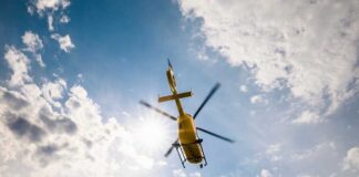 A yellow helicopter flying against a backdrop of clouds and sunlight
