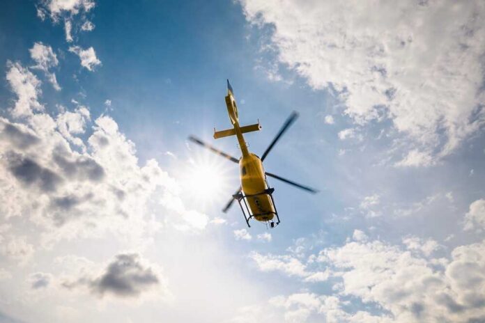 Flying,Helicopter,Of,Emergency,Medical,Service,On,Sky,On,Sunny A yellow helicopter flying against a backdrop of clouds and sunlight