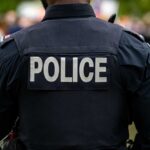 Back view of a police officer wearing a uniform with 'POLICE' displayed