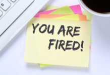 A sticky note with the message 'YOU ARE FIRED!' placed on a desk next to a keyboard and a cup of coffee