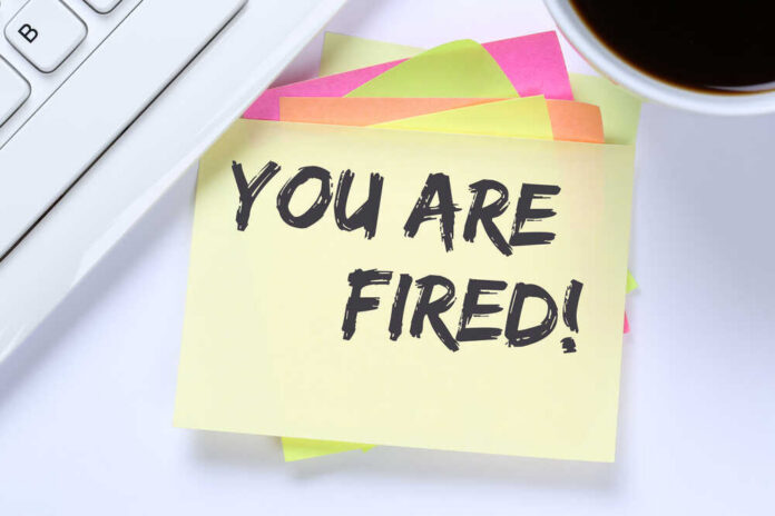 A sticky note with the message 'YOU ARE FIRED!' placed on a desk next to a keyboard and a cup of coffee