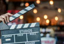 Evil Dead Icon Drops Chilling Cancer Timeline Hand holding a movie clapperboard in studio setting.