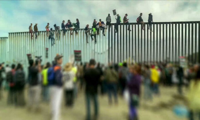 People sit atop a border wall during protest.