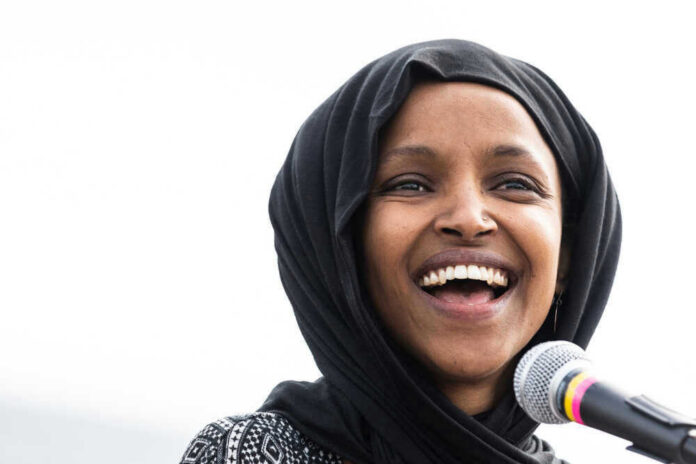 shutterstock_1369296272 Ilhan Omar with a black headscarf smiles near a microphone.