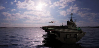 Aircraft carrier at sea with jet approaching to land