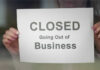 Giant COLLAPSES – Stores on Chopping Block A person holding a sign that reads 'CLOSED Going Out of Business'