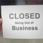 Giant COLLAPSES – Stores on Chopping Block A person holding a sign that reads 'CLOSED Going Out of Business'