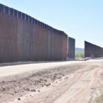 Dirt road beside tall metal border wall