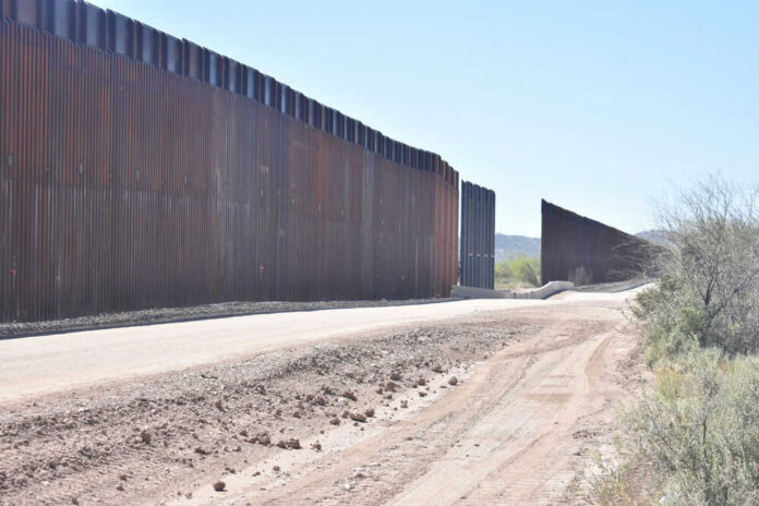 shutterstock_1958049433-1 Dirt road beside tall metal border wall