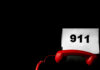 A red telephone next to a sign displaying the number 911 on a dark background