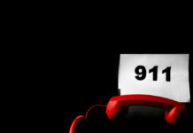 A red telephone next to a sign displaying the number 911 on a dark background