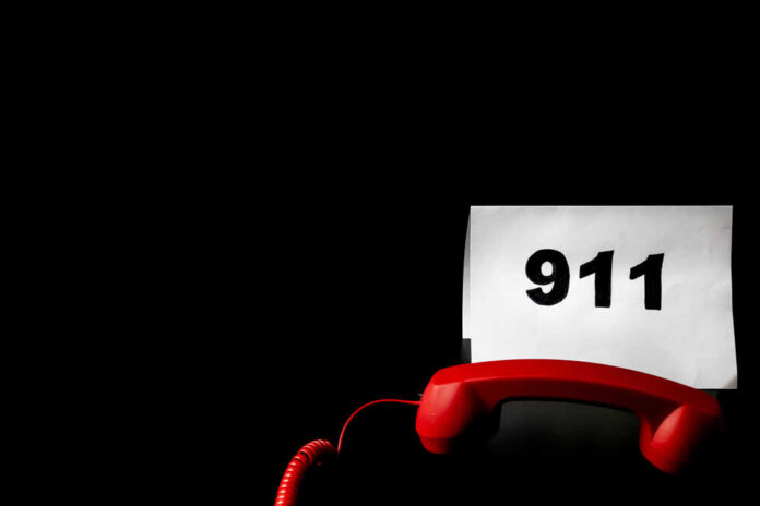 A red telephone next to a sign displaying the number 911 on a dark background