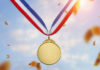 Gold medal with blue, white, red ribbon, sky background.