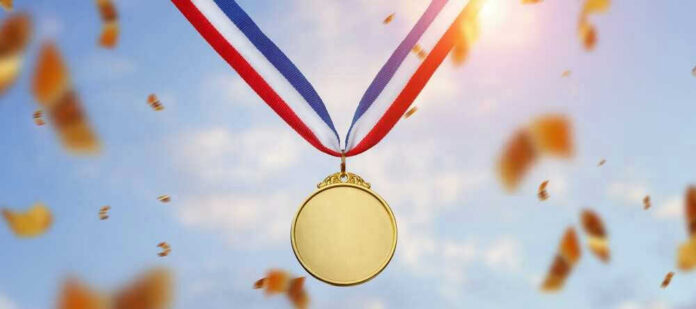 shutterstock_2219437071 Gold medal with blue, white, red ribbon, sky background.