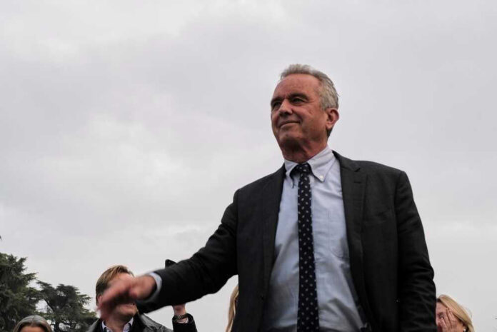 shutterstock_2314907207 Robert F. Kennedy Jr. in a suit stands outdoors, cloudy sky background.