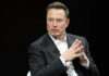 Musk Drops MASSIVE Giveaway Man in suit, hands clasped, black background.