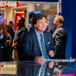 Tucker Carlson SLAMMED – Should He Apologize? Tucker Carlson at a news desk with audience clapping in studio