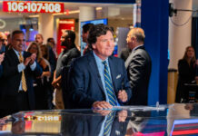 Tucker Carlson at a news desk with audience clapping in studio