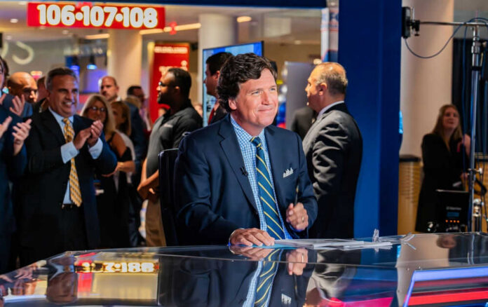 Tucker Carlson at a news desk with audience clapping in studio