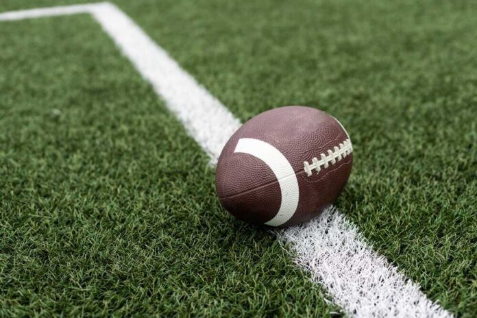 Football,On,Hash,Marks,Of,High,School,Turf,Football,Field American football resting on a white yard line on a turf field