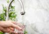 Hand holding a glass under a kitchen faucet as water pours in