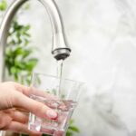 Families Blindsided by Soaring Water Tabs Hand holding a glass under a kitchen faucet as water pours in