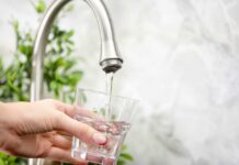 Families Blindsided by Soaring Water Tabs Hand holding a glass under a kitchen faucet as water pours in