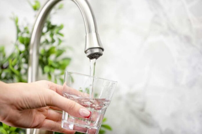 Water,Saving,Concept.,Woman,Filling,Glass,With,Tap,Water,Indoors, Hand holding a glass under a kitchen faucet as water pours in