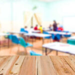 Teachers Bankroll Progressives Blurred classroom with students and a wooden foreground.